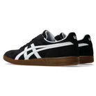 A pair of Gel Vikka Pro ASICS Black Brown 1201A486 Suede Skateboarding Shoes, featuring black suede uppers with white side stripes and brown rubber soles for optimal board control and comfort, displayed from rear and side angles against a plain white background.