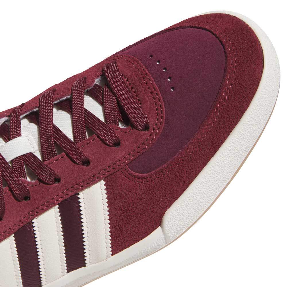 Close-up of the Glenburn Burgundy White KJ5048 Adidas Skateboarding Shoes, showcasing a maroon suede sneaker with white laces and a white sole. The shoe features three signature white stripes along the side and a classic suede texture around the toe area, emphasizing its timeless skateboarding style.
