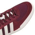 Close-up of the Glenburn Burgundy White KJ5048 Adidas Skateboarding Shoes, showcasing a maroon suede sneaker with white laces and a white sole. The shoe features three signature white stripes along the side and a classic suede texture around the toe area, emphasizing its timeless skateboarding style.