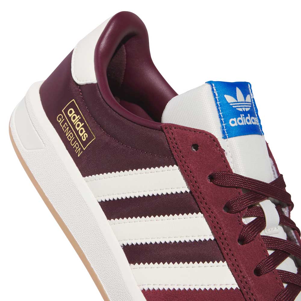 A close-up of the Glenburn Burgundy White KJ5048 Adidas Skateboarding Shoes highlights their classic silhouette with white stripes, a blue Adidas tongue label, black laces, and a gold Adidas Glenburn detail on the side—an iconic maroon sneaker perfect for any collection of adidas skateboarding shoes.