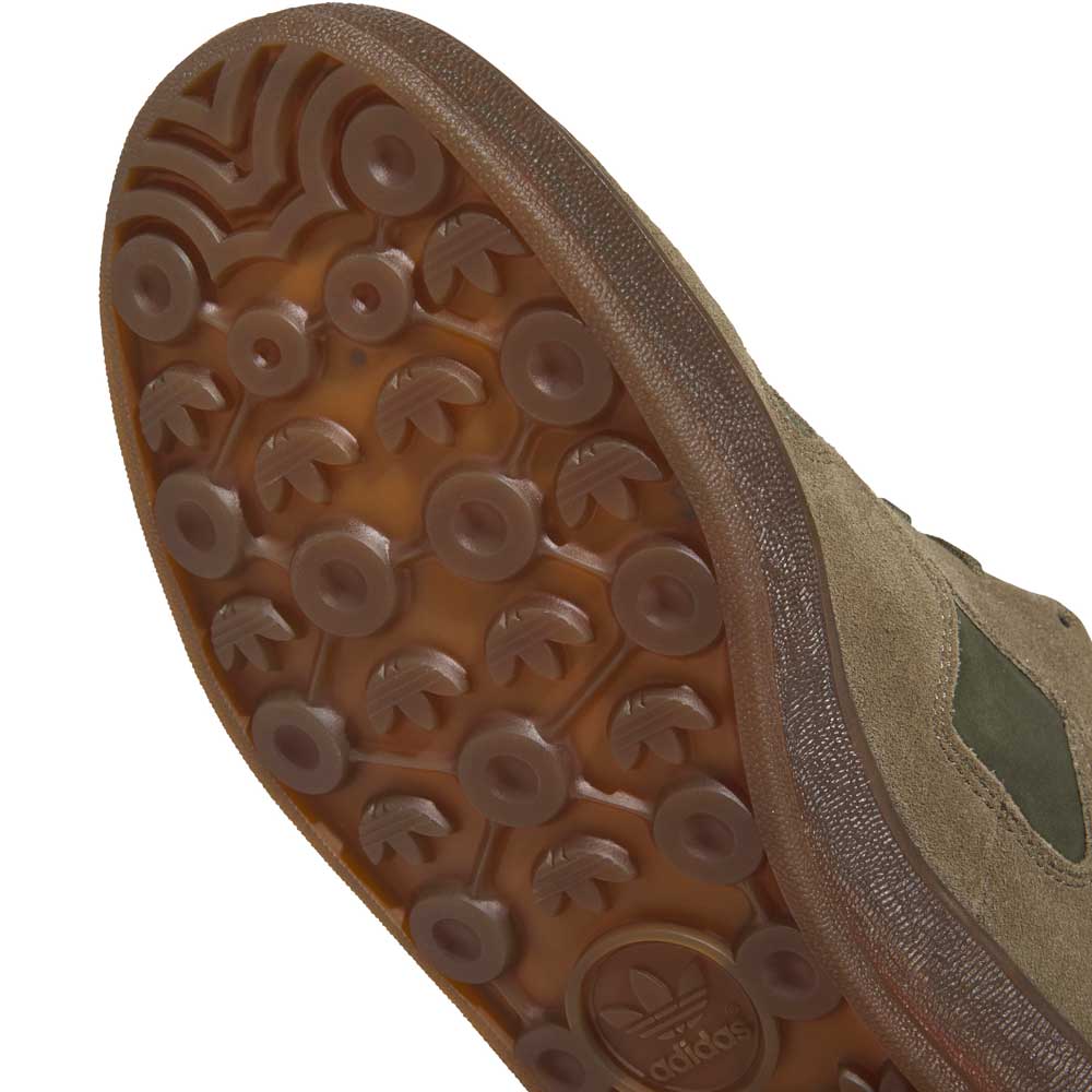 Close-up of the sole of a gray and black adidas Mark Gonzales KJ0281 Aloha Super Suede Skateboarding shoe, featuring a textured rubber pattern with circular and arrow-shaped treads and the Adidas logo. These skate-inspired trainers have a suede upper for enhanced durability and style.