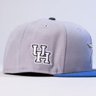 The Peoples Champ Gray Blue Houston Cougars New Era Hat 5950 Fitted features a light gray design with a blue brim and an embroidered white UH logo outlined in black on the side, showcasing classic Houston Cougars style.