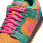 Close-up of the Nike SB Dunk Low Pro "Green Noise Watermelon Light Curry" HQ1625301 skateboarding shoe, featuring orange and green suede overlays, bright pink laces, pink leather upper with Swoosh, black midsole, and orange outsole.