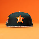 The Greenhand RTC Oil Houston Astros New Era Hat 5950 Fitted is a green fitted cap with the Astros H star logo, orange embroidery, and a patterned flat brim, shown on an orange background.