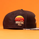The Old Head RTC Wood Oil Houston Astros New Era Hat 5950 Fitted is a black cap featuring a sunset design, "Houston Texas" on the side, and a unique patterned brim—ideal for any Houston Astros hat collector.