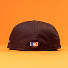 The Old Head RTC Wood Oil Houston Astros New Era Hat 5950 Fitted is shown from the back with an MLB logo patch, set against an orange background—a must-have cap for fans.