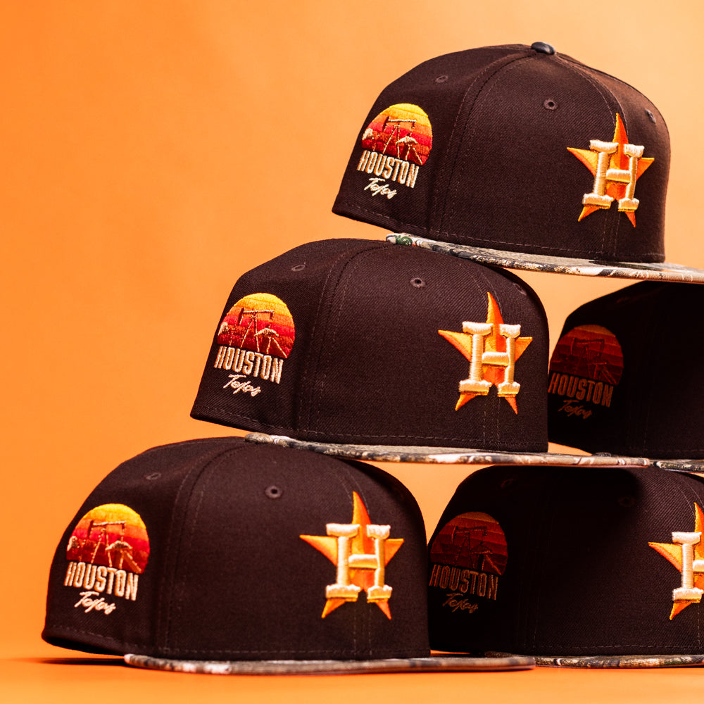 A stack of Old Head RTC Wood Oil Houston Astros New Era Hat 5950 Fitted caps, each with orange and yellow embroidered logos and a sunset graphic, arranged on an orange background—ideal for fans who love bold, standout style.