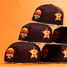 A stack of Old Head RTC Wood Oil Houston Astros New Era Hat 5950 Fitted caps, each with orange and yellow embroidered logos and a sunset graphic, arranged on an orange background—ideal for fans who love bold, standout style.