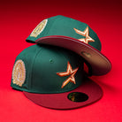 Two La Virgencita Green Red Gold New Era Houston Astros 5950 Fitted hats are stacked on a red surface. Each cap features a green crown, maroon brim, gold star patch on the front, and Virgen-inspired embroidered details on the side that celebrate Mexican culture.