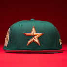 A La Virgencita Green Red Gold New Era Houston Astros Hat 5950 Fitted featuring a green crown with a gold star emblem on the front, maroon brim, gold logo details on the side, and set against a red background. This hat draws inspiration from Mexican culture and Virgen motifs, blending classic style with unique accent details.