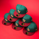 Six La Virgencita Green Red Gold New Era Houston Astros 5950 fitted hats are stacked in a pyramid shape on a bright red background, blending classic style with Mexican culture reminiscent of a Virgen-inspired design.