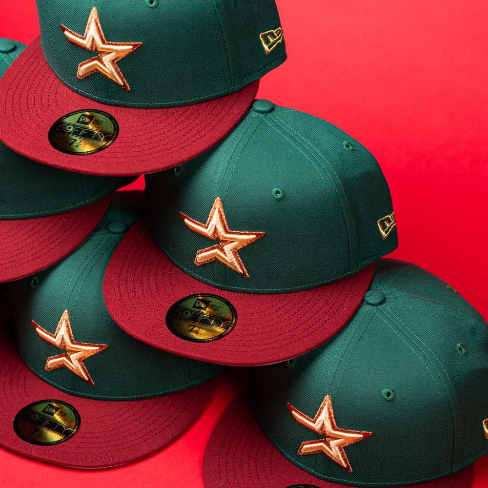 A stack of La Virgencita Green Red Gold New Era Houston Astros Hat 5950 Fitted baseball caps, featuring gold star logos and New Era stickers on the visors, inspired by designs that celebrate Mexican culture, set against a bright red background.