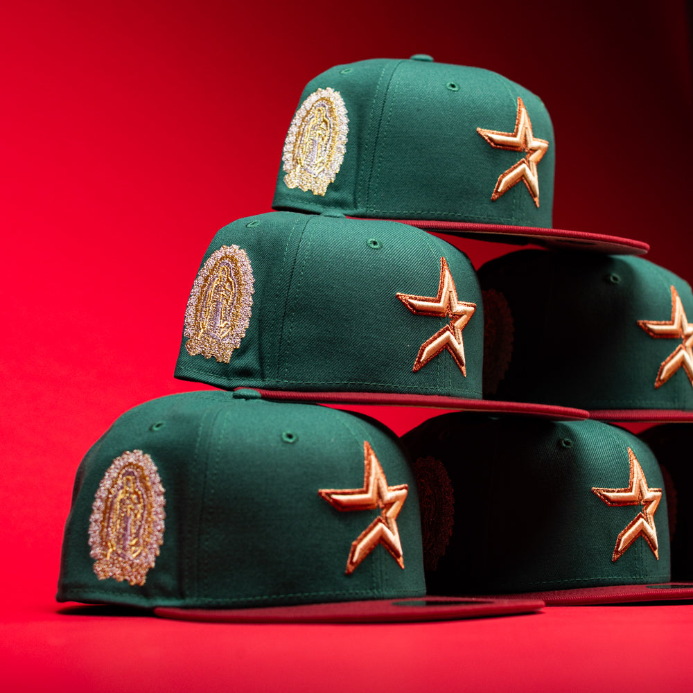 Five La Virgencita Green Red Gold New Era Houston Astros 5950 Fitted hats, inspired by Mexican culture and classic La Virgencita designs, are stacked in a pyramid on a bright red background.