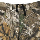 Close-up of the Groundwork 2 Cargo Pants Realtree APX Bottom Mens Independent, a camouflage-patterned ripstop cargo pant featuring belt loops, a black drawstring, button closure, and front pockets; designed in the Realtree APX colorway of brown, green, and tan for durable style inspired by Independent Trucks apparel.