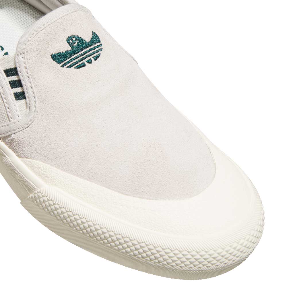 Close-up of the HQ4721 Gray White Shmoofoil Slip RX Adidas Skateboarding Suede Shoes, featuring a textured white rubber toe cap and signature green logo near the tongue, showcasing their comfort and style.
