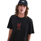A person with long, curly hair wears a black Nike SB cap and the HV2195010 Max 90 Skate T-Shirt — a black, midweight cotton tee with a red Nike SB graphic on the front—standing against a plain white background.