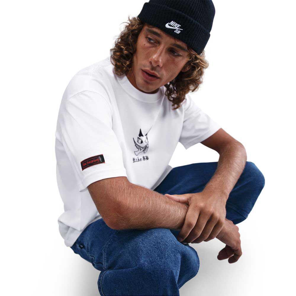 A person with curly hair wears a black Nike beanie, blue jeans, and the HV2195100 Max 90 Skate T-Shirt SB Tee—a midweight, white Nike SB skateboarding tee with screenprinted graphics—against a plain white background for daily comfort.