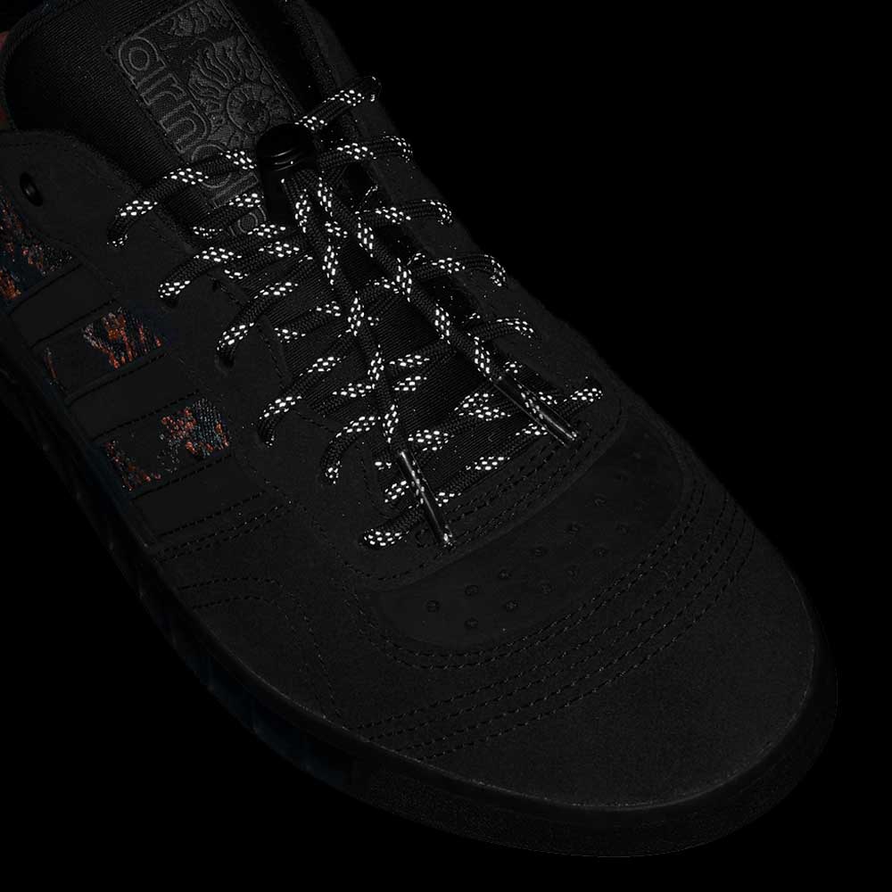 Close-up of the Handball Top x Mike Arnold Shoes: black suede Adidas skateboarding shoes with patterned laces, subtle red and orange side accents, and an Adidas logo by the tongue.