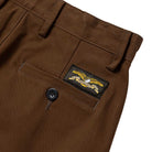 The Hecho Por Skate Pant by Anti Hero Skateboards in brown features a back pocket with a black button and a rectangular patch above it showing an eagle with arrows—ideal for Skateshop Day or celebrating exclusive skateboard drops.