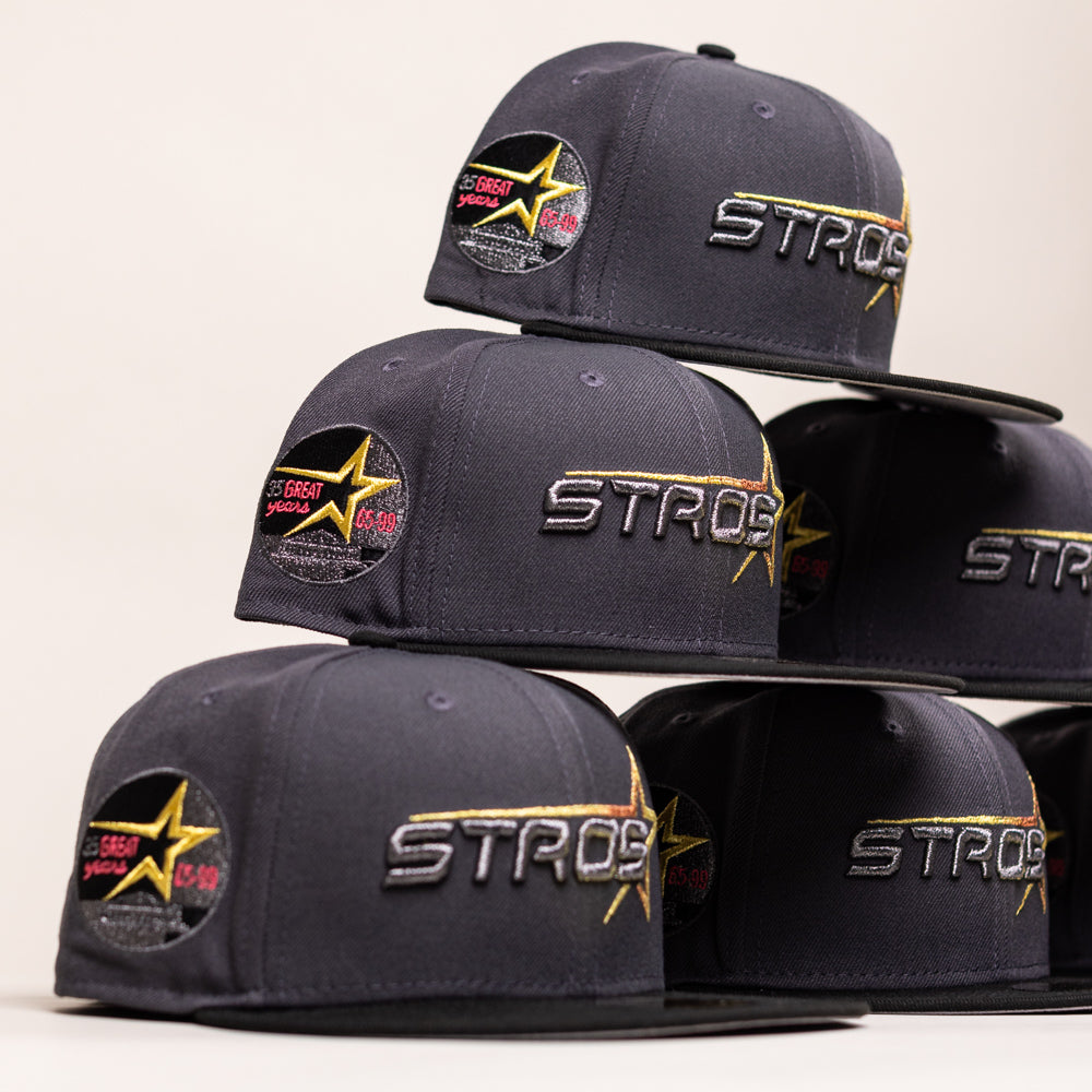 A stack of five charcoal gray Black Delta City Connect Houston Astros New Era Hat 5950 Fitted caps, each featuring ASTROS embroidered in silver and gold on the front and a commemorative star-shaped patch on the side.