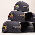 A stack of five charcoal gray Black Delta City Connect Houston Astros New Era Hat 5950 Fitted caps, each featuring ASTROS embroidered in silver and gold on the front and a commemorative star-shaped patch on the side.
