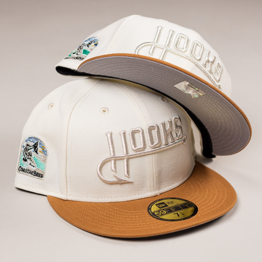 Two white The Hookset Corpus Christi Hooks New Era Hat 5950 Fitted caps with tan brims and embroidered team logos are stacked. Each has a coastal bird side patch and a gold size 7 1/4 sticker on the brim.