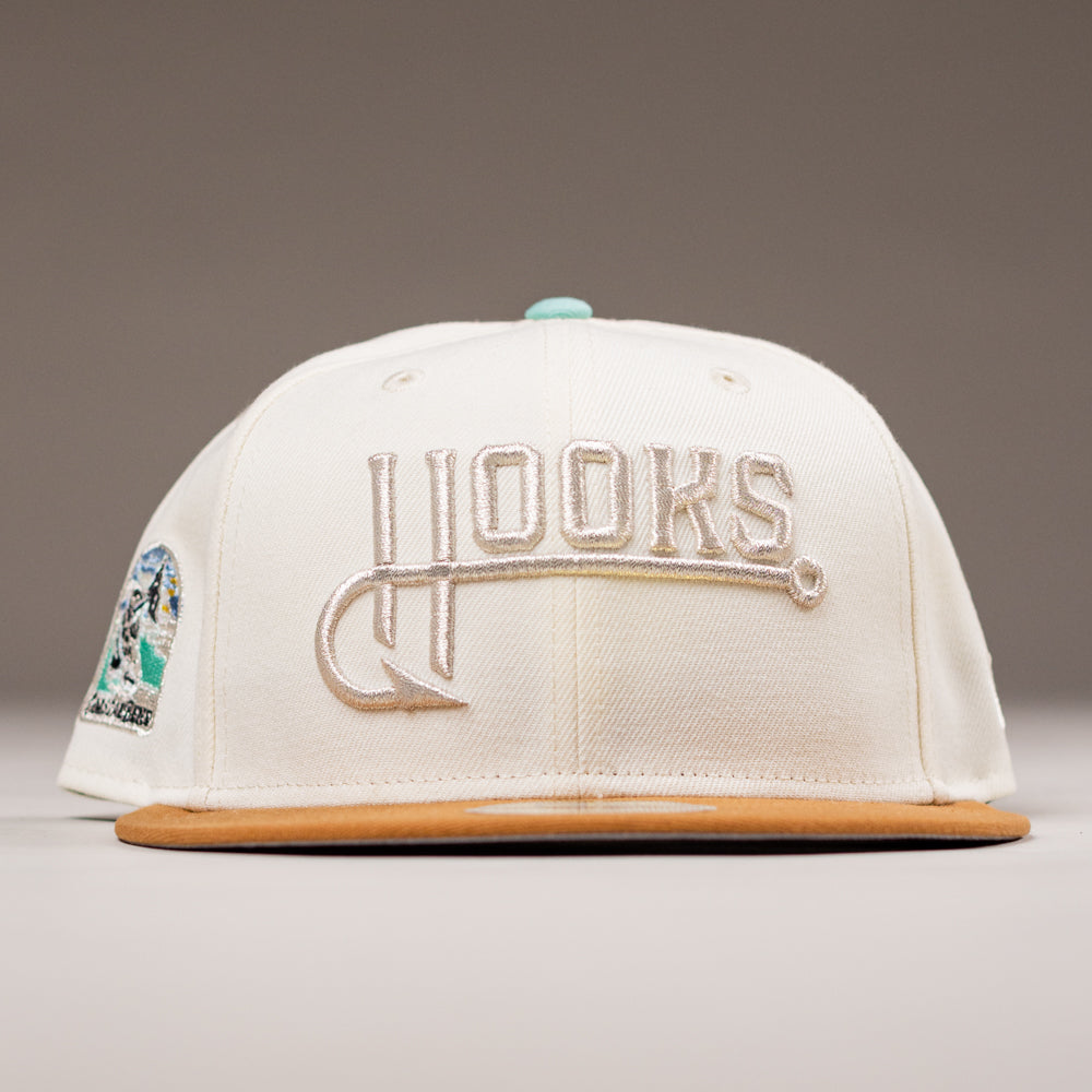The Hookset Corpus Christi Hooks New Era Hat 5950 Fitted features a cream crown, tan brim, HOOKS (H as a fish hook) embroidered in front, and a colorful side patch celebrating the Corpus Christi Hooks.
