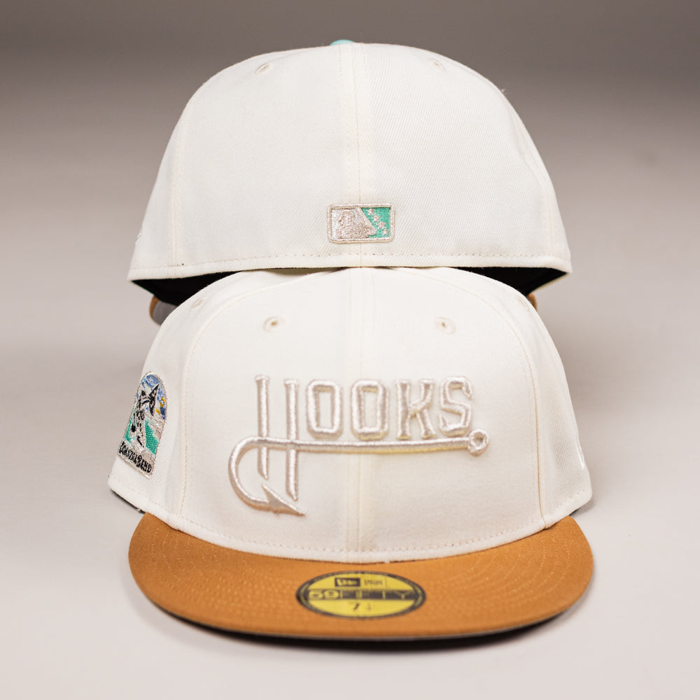 Two white The Hookset Corpus Christi Hooks New Era 5950 Fitted Hats with brown brims are shown. "Hooks" is embroidered in tan and white on the front, a teal and silver logo is on the back, and a colorful side patch is visible.