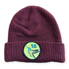 The Hummingbird Beanie Maroon TU Transportation Unit is a soft acrylic knit with a folded brim and a front patch showing a blue and white bird with "T.U." on a light green background.