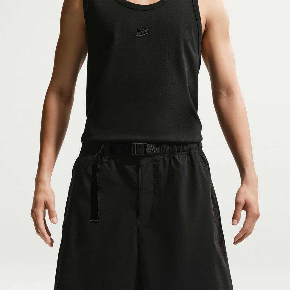 Wearing a black sleeveless Nike tank top and IF1096010 Black White Skate Shorts Nike SB, a person stands against a plain light background, arms relaxed at their sides, highlighting a skate-ready look.