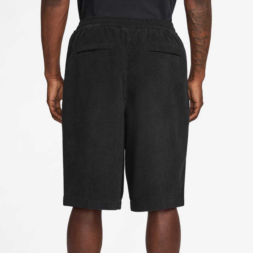 A person wearing II4426010 Black White Corduroy Skate Shorts Nike SB is shown from the back, highlighting the elastic waistband and two back pockets, standing against a plain light background.
