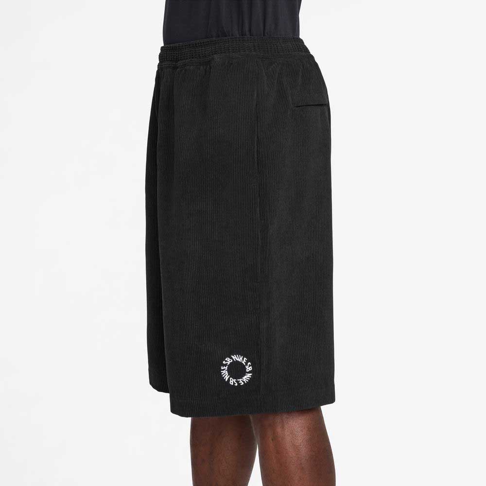 A person wears II4426010 Black White Corduroy Skate Shorts by Nike SB, featuring an elastic waistband and a small white circular logo near the hem, standing against a plain white background.