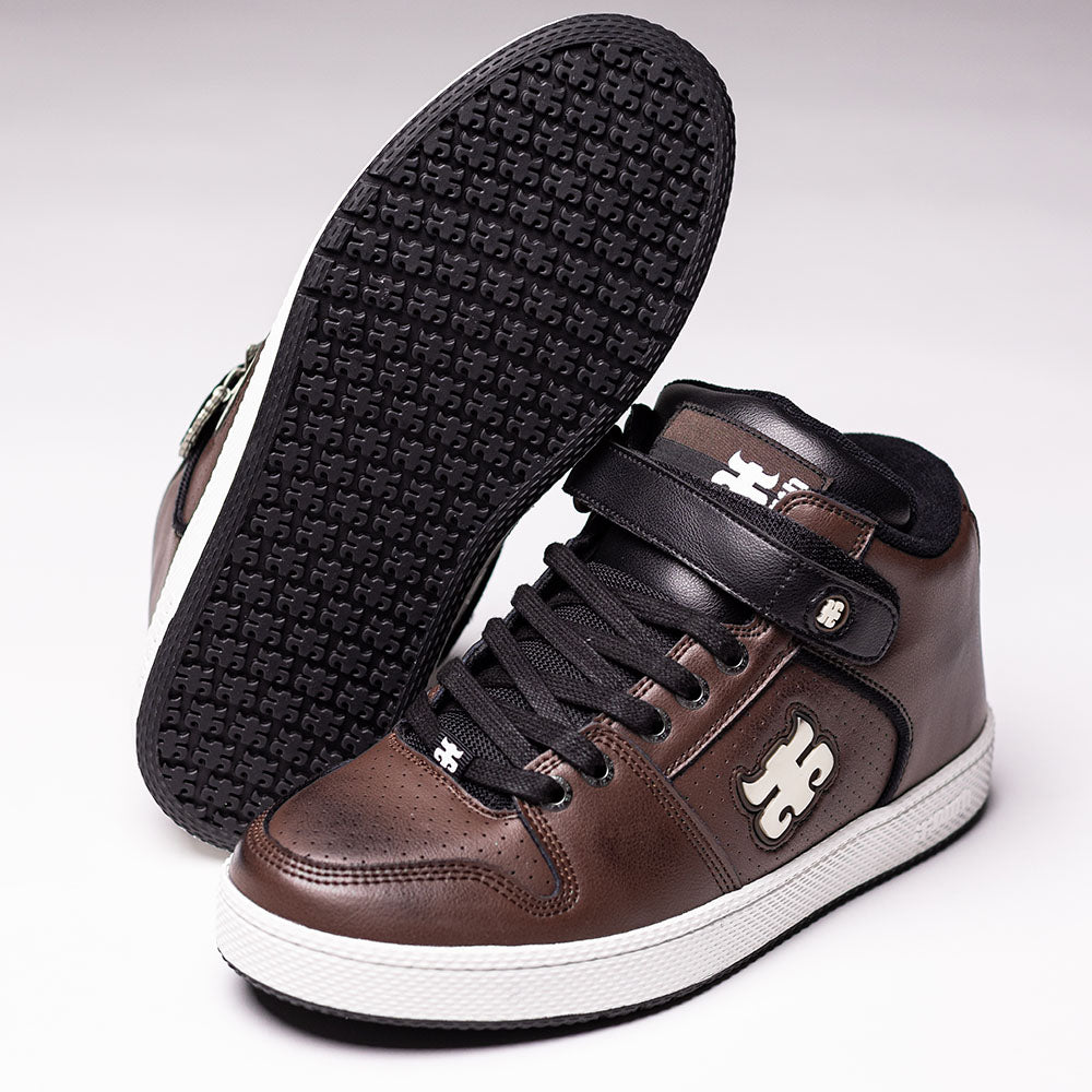 A pair of Grasshopper Brown Leather I Path Shoes Skateboarding, crafted from brown and black suede with white soles and a white logo on the side. These mid-top sneakers feature an Ortholite insole for added comfort. One shoe is displayed upright while the other lies sideways, highlighting the textured sole.