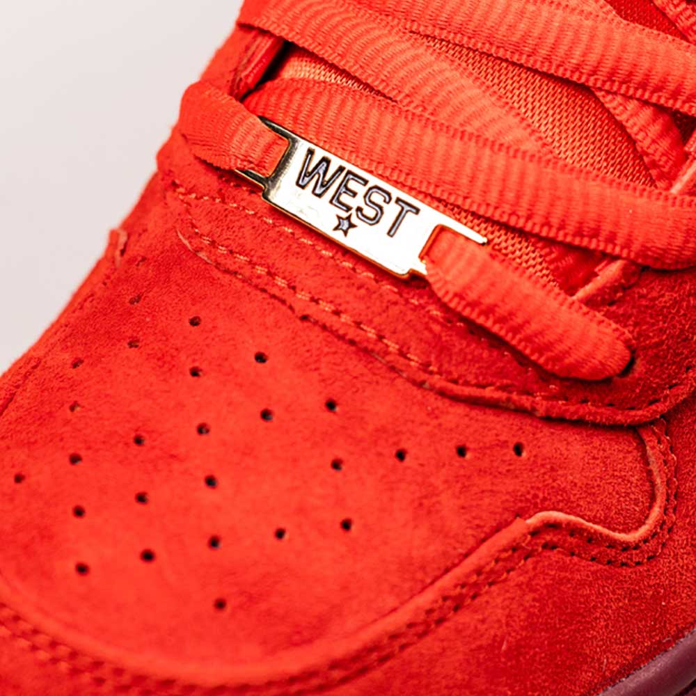 Close-up of the IQ5648600 Habanero Red Club Gold Team Red Paul Rodriguez Zoom Air Low Nike SB suede skateboarding shoe, featuring matching laces, a gold WEST lace lock, perforated toe box, leather upper, and durable traction details.