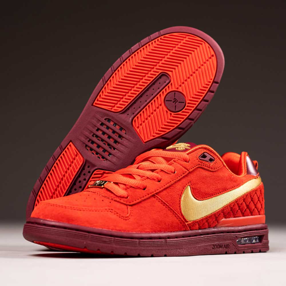 A pair of IQ5648600 Habanero Red Club Gold Team Red Paul Rodriguez Zoom Air Low Nike SB suede skateboarding shoes, with gold detailing and visible Air unit—one upright, the other on its side.
