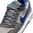 Close-up of the IU7835001 Flint Grey Deep Royal Blue Paul Rodriguez Zoom Air Low Suede Skateboarding Shoes, featuring a gray suede upper, blue Nike swoosh and tongue detail, gray laces, perforated texture, and Air Zoom cushioning for comfort.