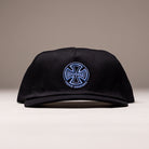 A black Independent Skateboards Truck Co Legacy unstructured snapback hat with a tan brim, featuring the embroidered logo on the front, shown against a neutral background. Unisex, one size fits most.