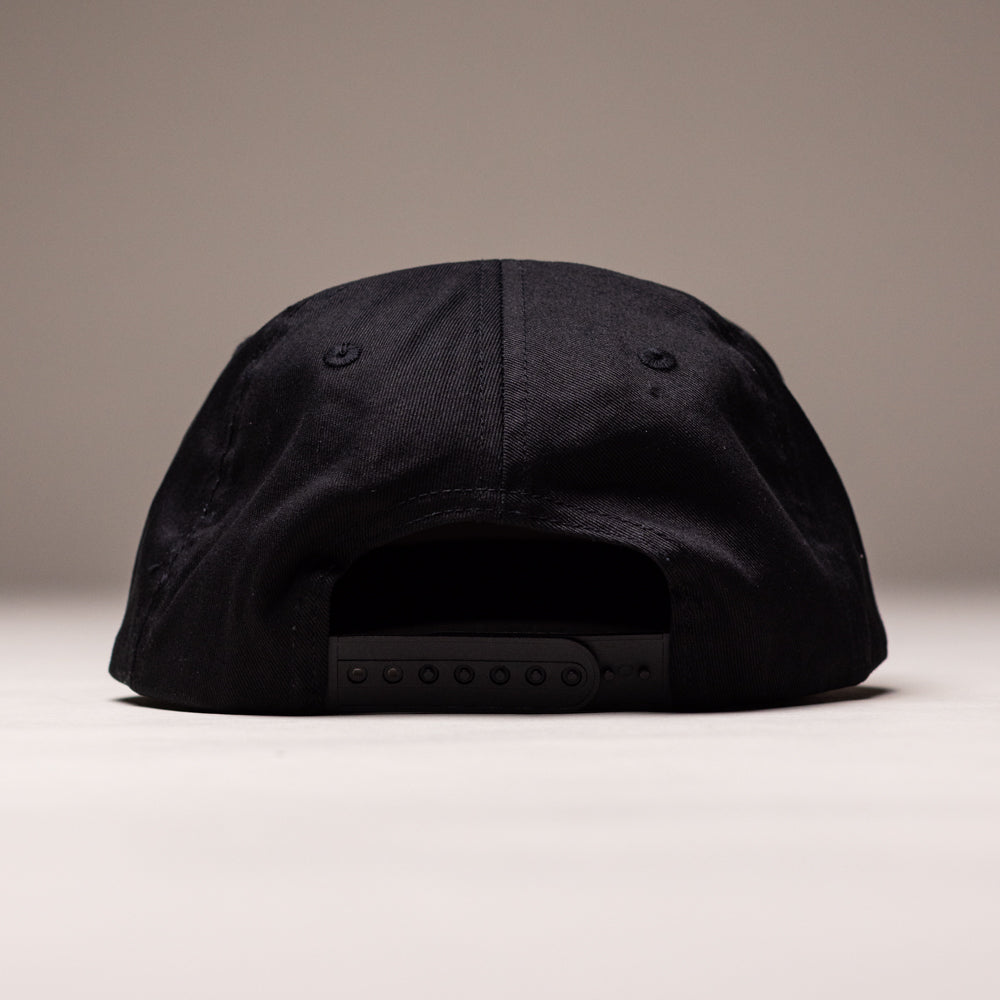 The Truck Co Legacy Black Hat by Independent Skateboards is a unisex, unstructured, low-profile tan snapback with visible stitching and an adjustable strap, shown from the back on a plain neutral background.