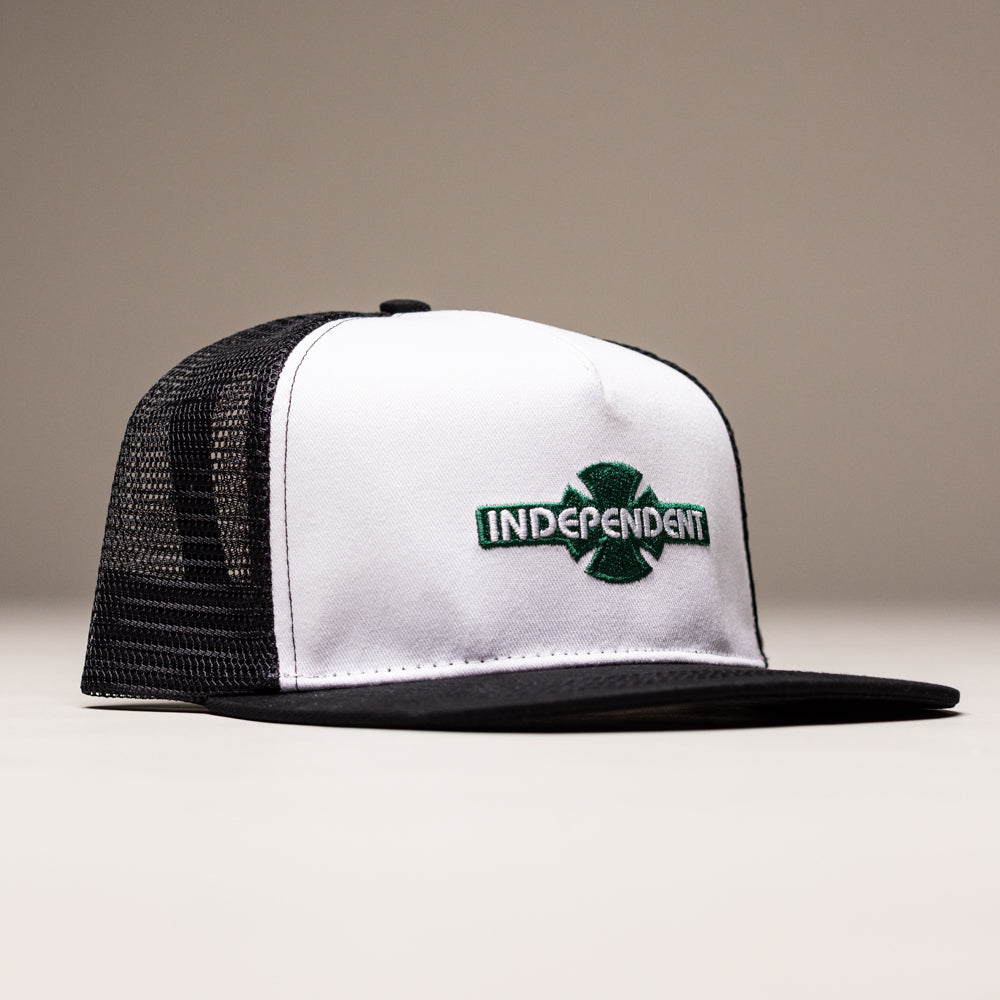 The OGBC Legacy White Dark Green Hat is an unstructured snapback with a mesh back, flat black brim, and cotton twill. It features a green cross logo and "INDEPENDENT" embroidered in green/black on the front. Unisex, by Independent Skateboards.