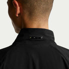 A person with short hair is shown from behind wearing a black Nike SB Ishod Cargo Track Jacket (IF0438010); a small rectangular device labeled WAIR is attached to the jacket’s collar.