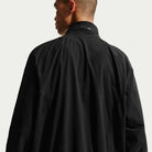 A person with short hair is seen from behind, wearing a black Ishod Cargo Track Jacket Black IF0438010 by Nike SB with a high collar, set against a plain light background.