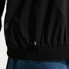 Close-up of a person wearing the Nike SB Ishod Cargo Track Jacket Black IF0438010 with perforated details, elastic waistband, and a small Nike tag, styled with blue denim jeans.