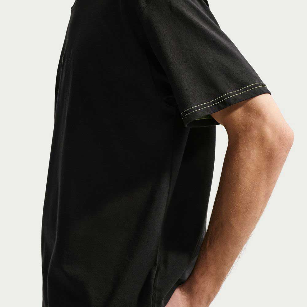 A person in a short-sleeved Ishod Tee Black IH1437010 Nike SB T-Shirt made from midweight cotton stands sideways, hand on hip, against a plain light background.