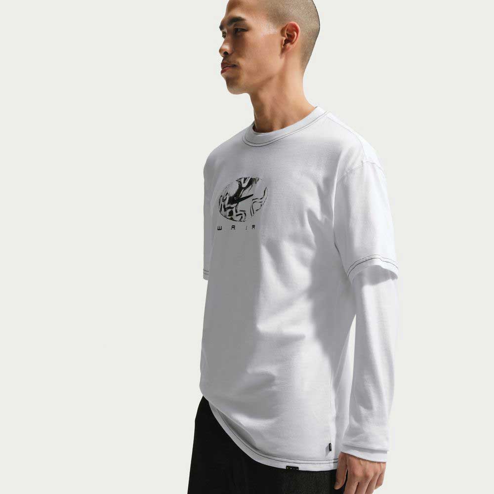 A person with a shaved head models the Ishod Tee White IH1437100 Nike SB T-Shirt, a midweight cotton top with a black abstract chest graphic, standing against a plain background for an effortless Ishod Wair-inspired look.