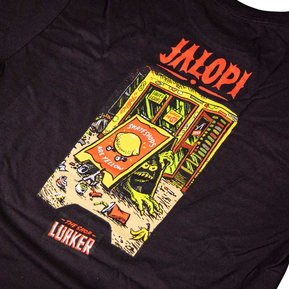 Black tee by Anti Hero Skateboards featuring a colorful Jalopi shop illustration for Skateshop Day. A green creature lurks inside; outside, a sandwich board reads "Smartshops are not yellow." Text at bottom: "The Shop Lurker.