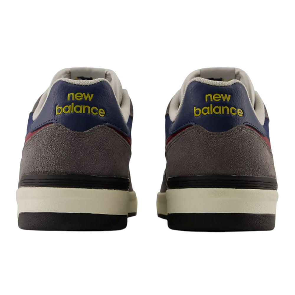 A pair of Jamie Foy Cup 306 CON New Balance Numeric Suede Skateboarding Shoes viewed from the back, featuring the brand’s yellow logo on gray, durable suede heels with navy, white, and red accents—designed for impact protection inspired by Jamie Foy skate shoes.