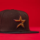 The KB2 OG Wood Black The Original Houston Astros New Era Hat 5950 Fitted features a gold and red outlined star emblem on the front, representing the Astros, all set against a bold black background.