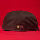 The KB2 OG Wood Black The Original Houston Astros New Era 5950 Fitted Hat is shown from the back against a red background, with a small embroidered logo in gold, red, and black near the bottom center of the cap.