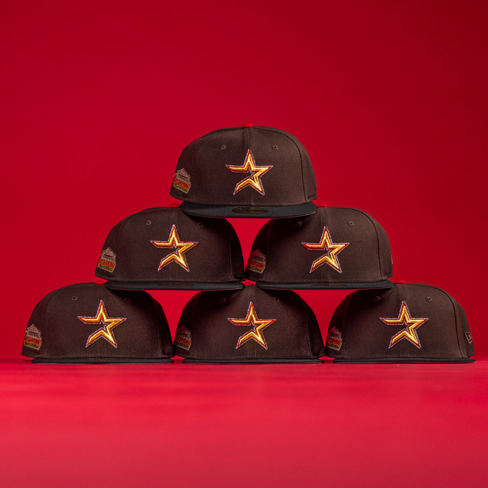 Six KB2 OG Wood Black The Original Houston Astros New Era Hat 5950 Fitted caps, each with a yellow and red star logo and a colorful side patch, are stacked in a pyramid against a solid red background.