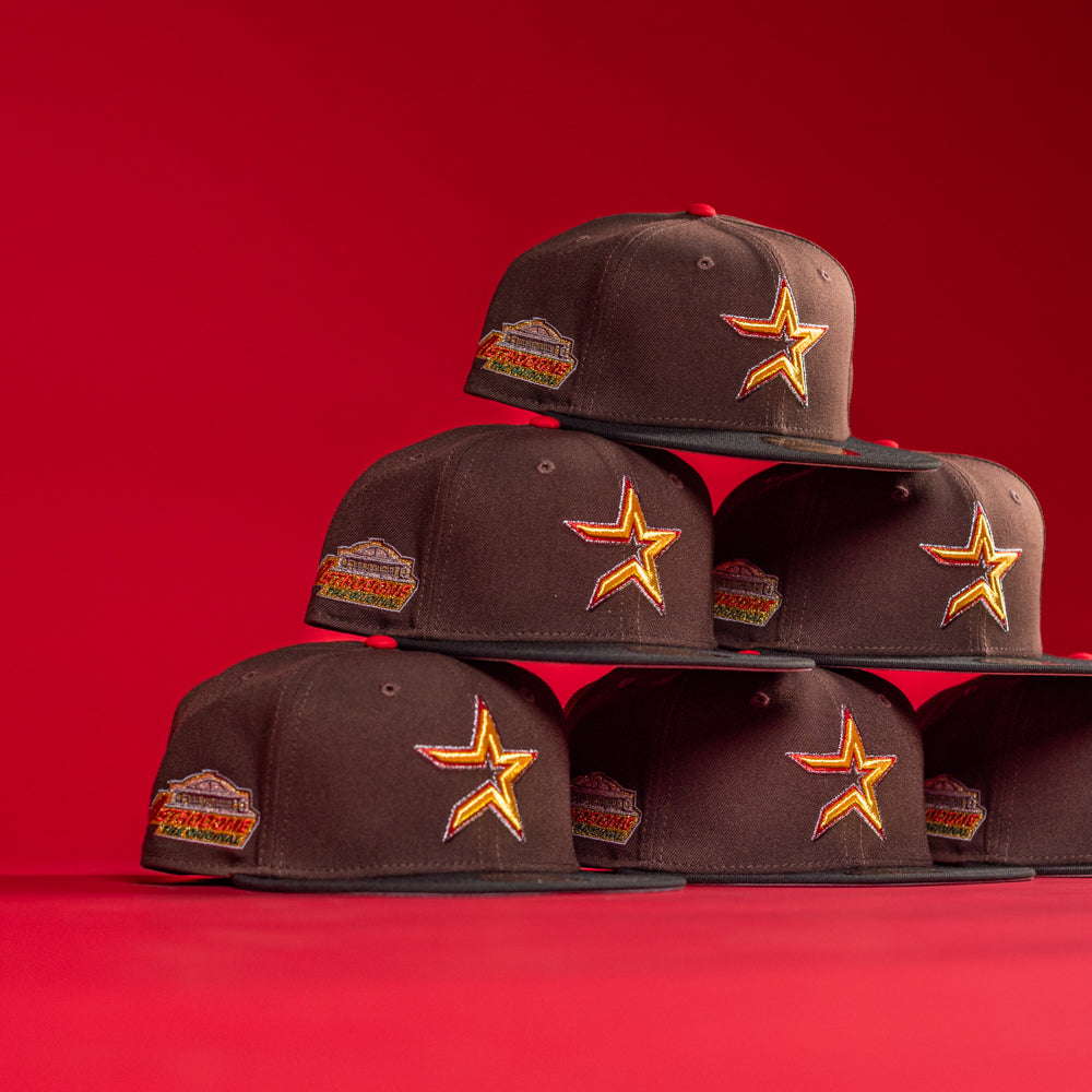 Six KB2 OG Wood Black The Original Houston Astros New Era Hat 5950 Fitted caps, each with a gold and red star logo and side patch, are stacked in a pyramid against a solid red background.
